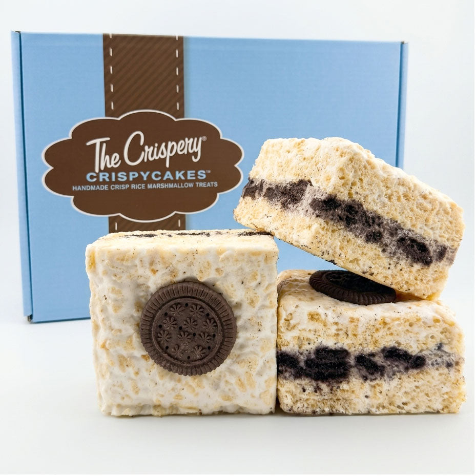 Three Cookies & Cream Crispycakes arranged in front of a blue Crispery gift box, showing chocolate cookie layers and cookie-topped treats.