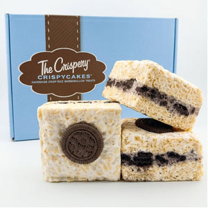 Three Cookies & Cream Crispycakes arranged in front of a blue Crispery gift box, showing chocolate cookie layers and cookie-topped treats.